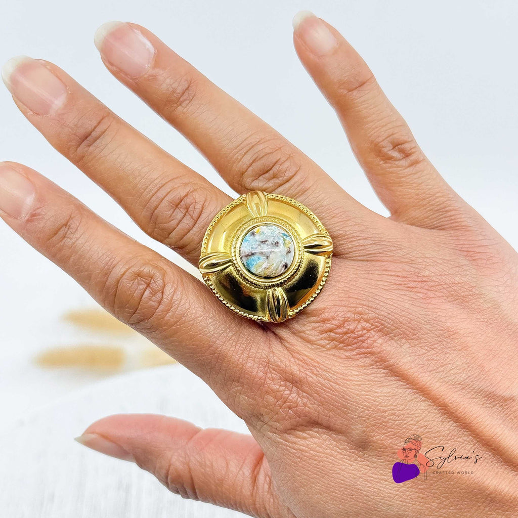 Bague dorée artisanale en argile polymère "Diane" portée sur une main, avec un design bouclier texturé et un centre marbré unique. Bijou fait main en France, élégant et original.