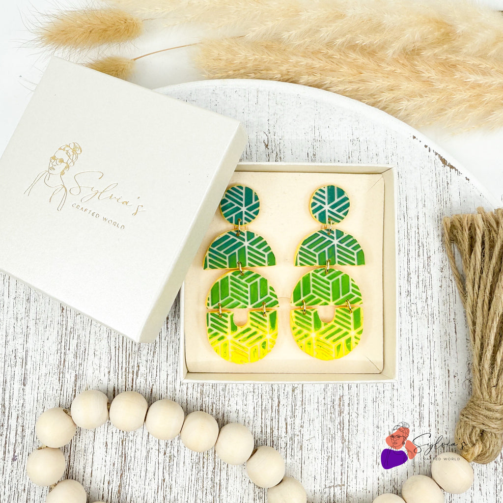 Boucles d’oreilles artisanales en argile polymère vertes et jaunes à motifs géométriques, présentées dans une boîte cadeau Sylvia’s Crafted World – bijoux faits main modernes et colorés.