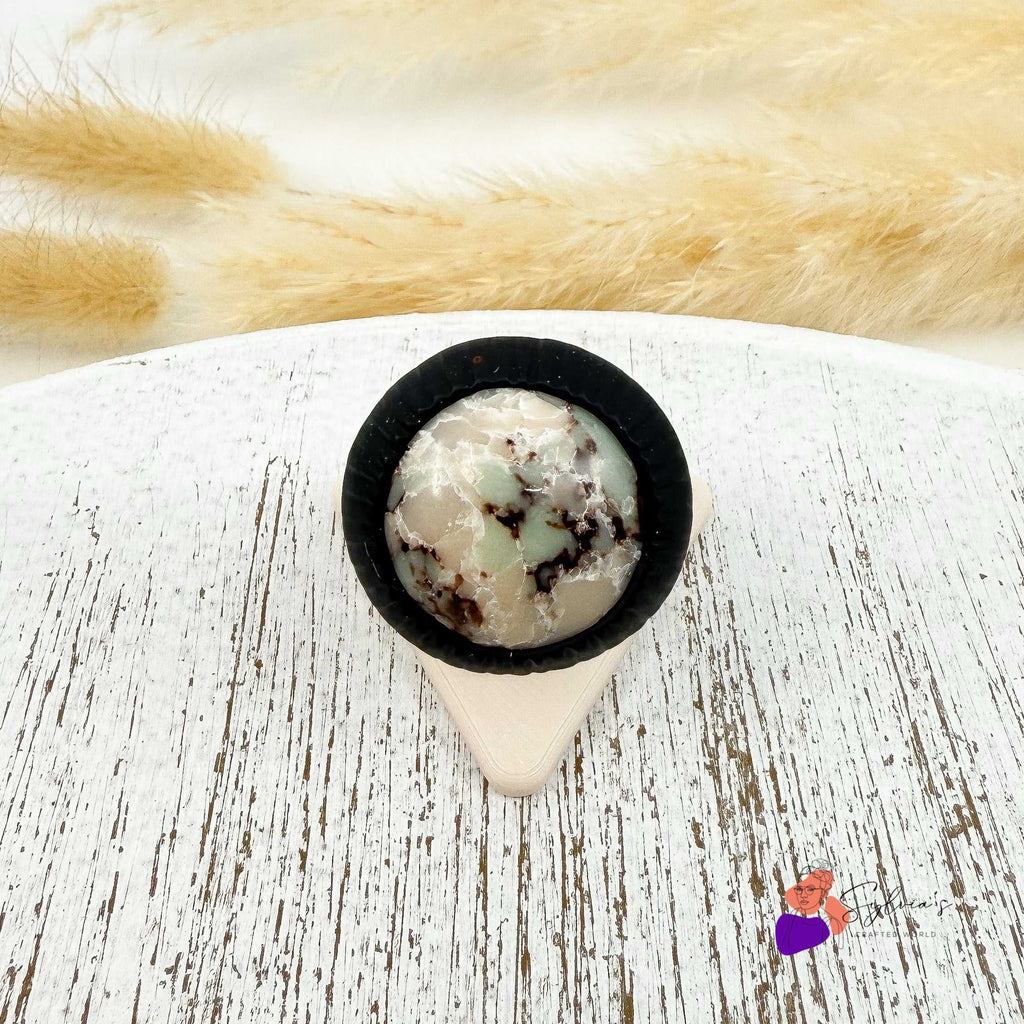 Bague artisanale noire en argile polymère 'Freyja' avec motif minéral, bijou unique pour femme, posée sur support en bois clair.