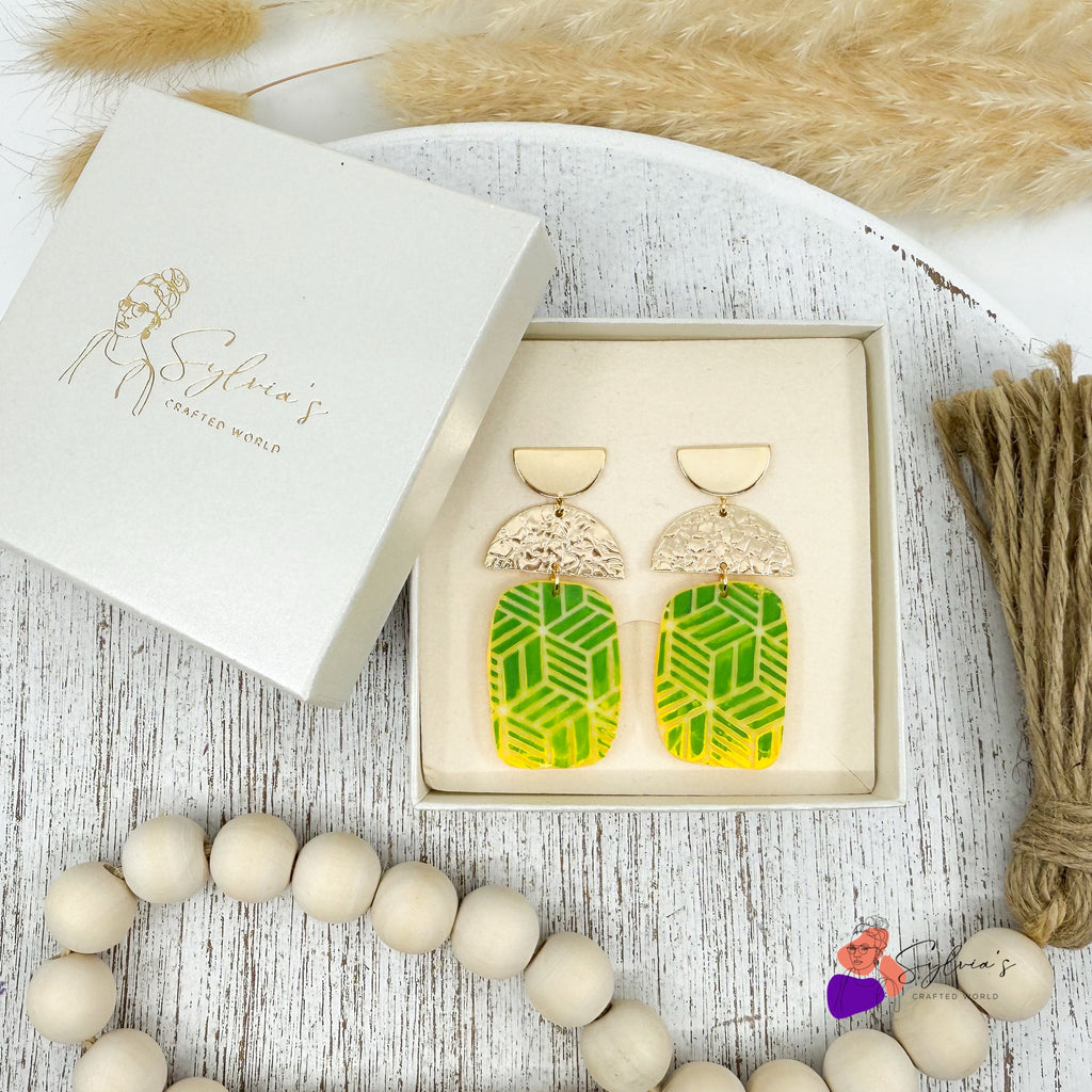 Boucles d’oreilles artisanales en argile polymère vertes et jaunes à motifs géométriques, demi-lunes dorées texturées, présentées dans une boîte cadeau Sylvia’s Crafted World – bijoux faits main modernes et élégants.