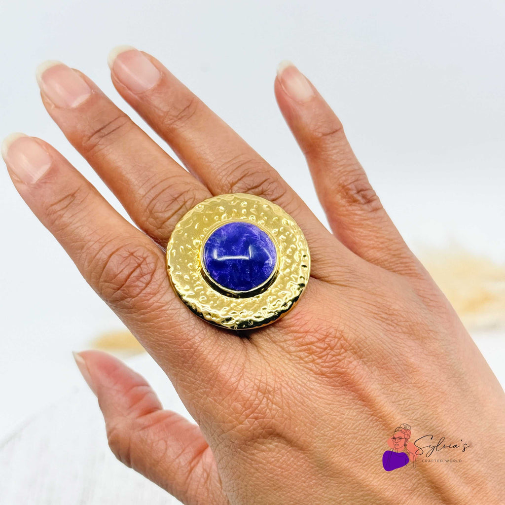 Bague artisanale Jacinthe en argile polymère avec plateau doré martelé et cabochon bleu, portée sur une main féminine. Bijou unique fait main.