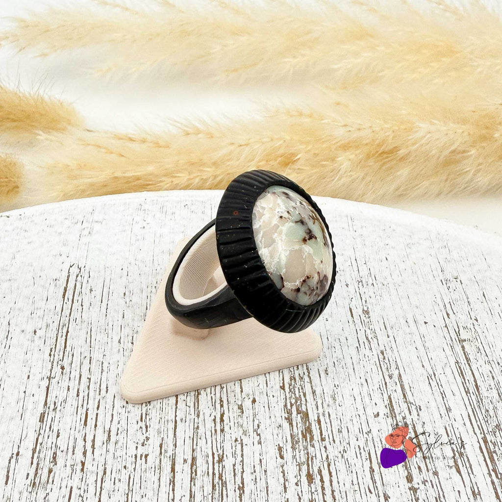 Bague artisanale noire en argile polymère 'Freyja' avec cabochon minéral, montée sur support réglable, posée sur présentoir en bois clair.