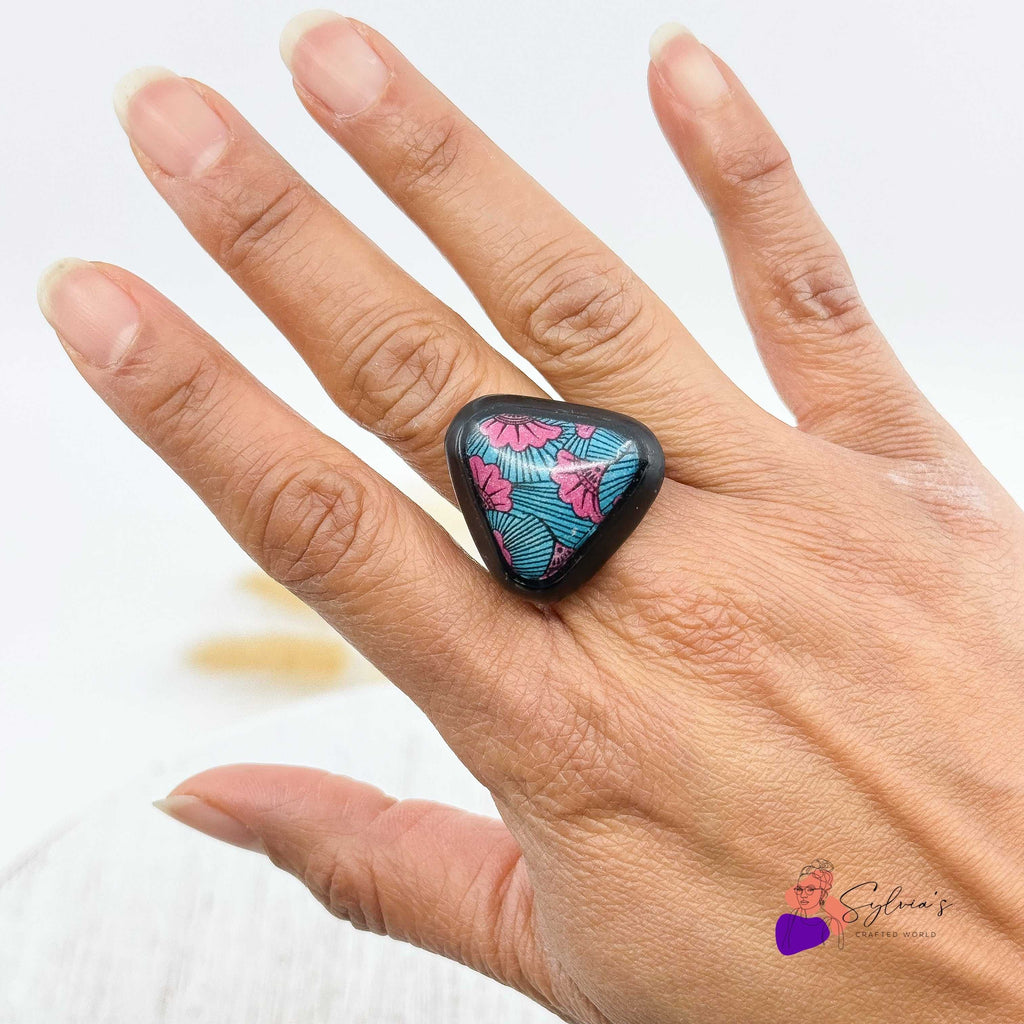 Bague artisanale motif wax en argile polymère 'Aya' aux couleurs vives bleu et rose, portée sur une main, bijou original et ethnique.