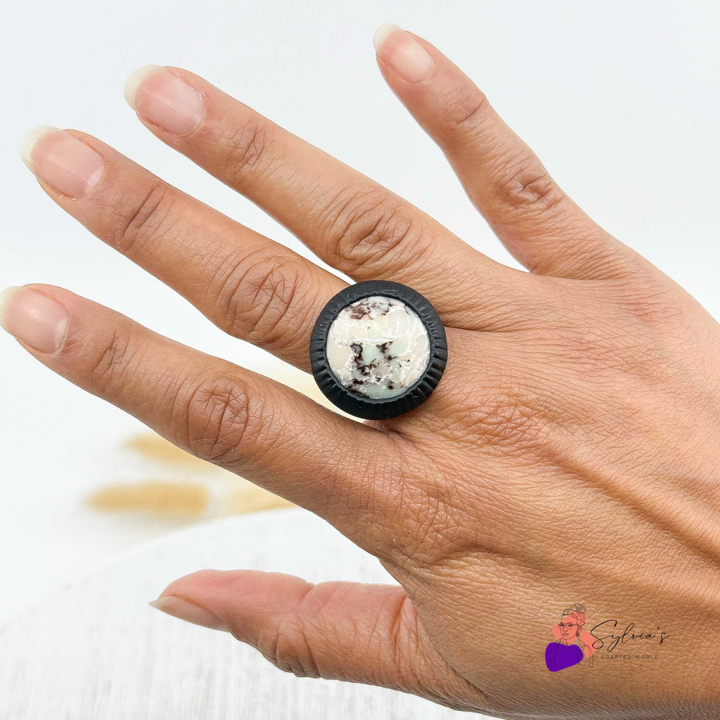 Bague artisanale noire en argile polymère 'Freyja' portée sur une main, avec cabochon central aux teintes minérales. Bijou unique fait main.