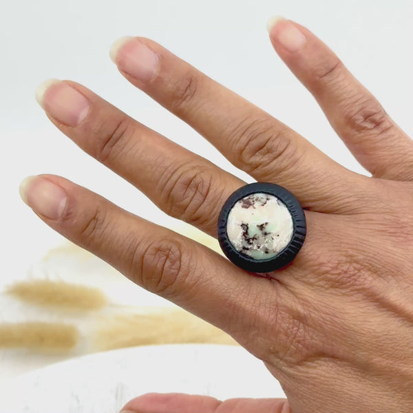 Bague artisanale noire en argile polymère 'Freyja' portée sur une main, avec un motif minéral central unique. Bijou fait main au style original.